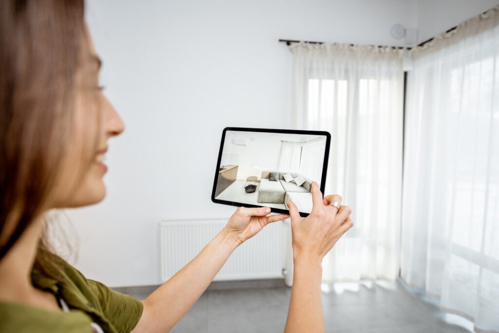 Mujer joven colocando muebles digitales con una tablet en el interior vacío de una habitación usando realidad aumentada.